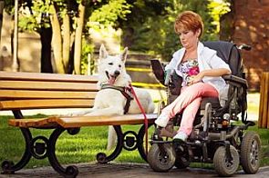 Agnieszka Filipkowska na wózku elektrycznym w parku, na ławce obok niej leży pies asystujący