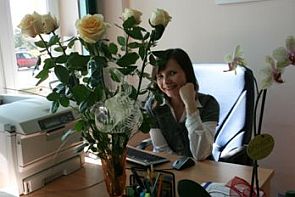 Anna Kopcińska-Wielgus siedzi za biurkiem, na pierwszym planie bukiet białych róż.
