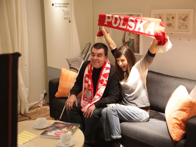 Roman Roczeń i Agnieszka Więdłocha kibicują przed telewizorem; zdjęcie z realizacji zdjęć do kampanii "Więcej nas łączy niż dzieli"