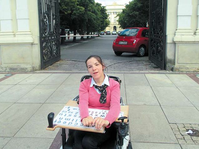 Agnieszka Bal siedzi na wózku przed bramą Uniwersytetu Warszawskiego