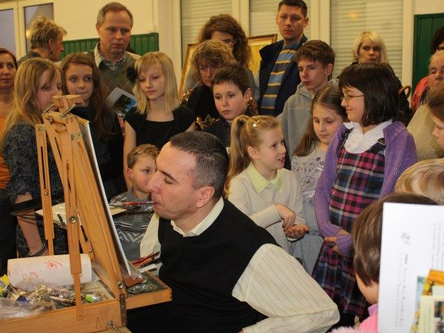 Mariusz Mączka maluje ustami obraz na oczach grupy dzieci i młodzieży