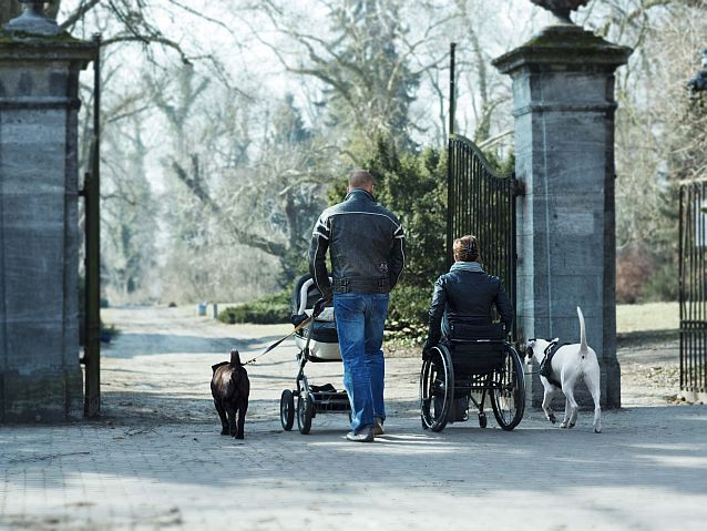 Mężczyzna z wózkiem dziecięcym i kobieta na wózku inwalidzkim na spacerze w parku