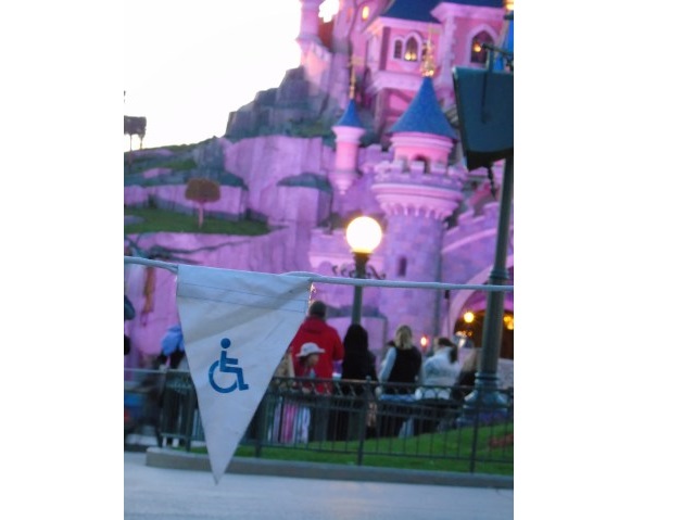 trójkąt z symbolem osoby z niepełnosprawnością powiewa na sznurku w tle różowego zamku w Disneylandzie, Paryż