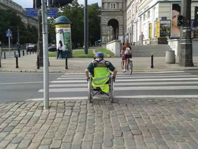 mężczyzna na wózku jedzie do przejścia dla pieszych po kostce