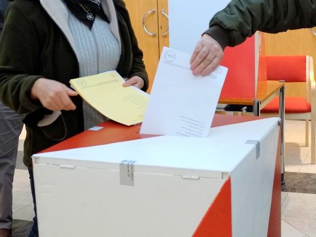 Dwie osoby wrzucają karty do głosowania do urny wyborczej
