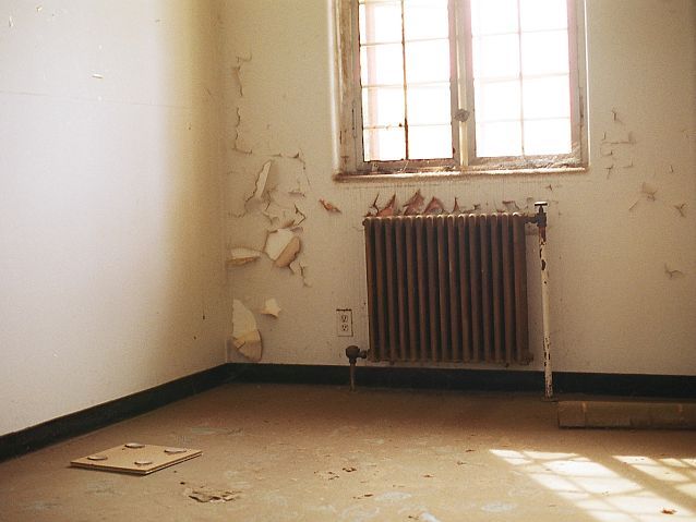 Odrapane ściany pokoju z kratą w oknie