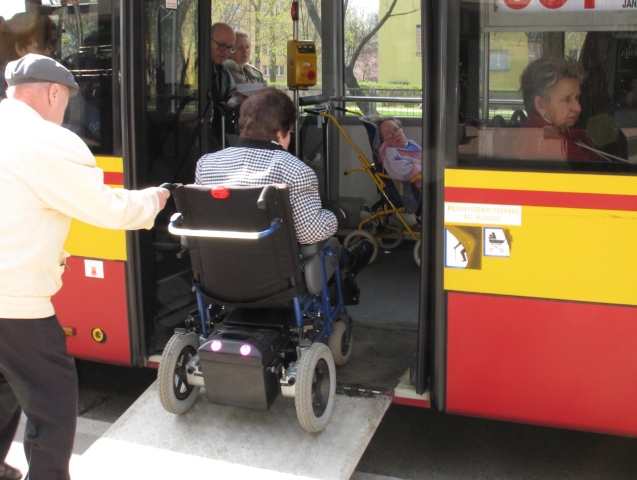 starszy mężczyzna pomaga wjechać do autobusu kobiecie na wózku inwalidzkim