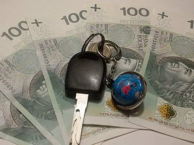 Banknoty, na których leżą kluczyki samochodowe z brelokiem w kształcie globusa
