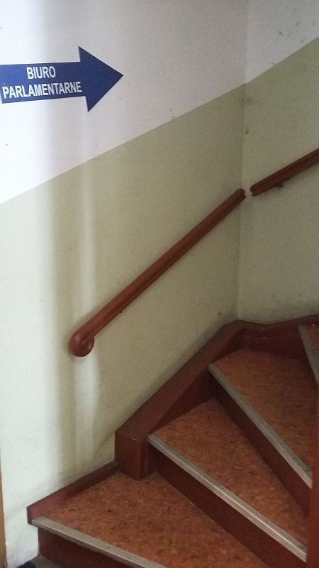 Kręte drewniane schody, nad którymi widnieje strzałka z napisem: biuro parlamentarne