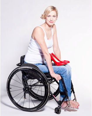 Magdalena Biegańska siedzi na wózku. Ma bose stopy, na kolanach stoją czerwone szpilki