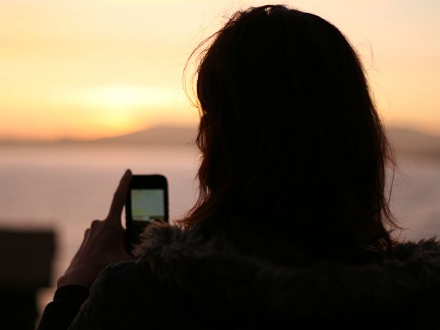 Dziewczyna z telefonem w rękach, w tle zachód słońca