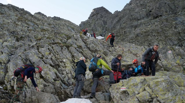 grupa osób sprawnych i z niepełnosprawnością wchodzi na skalny szczyt góry