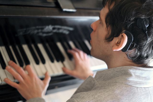 Grzegorz Płonka przy klawiaturze fortepianu. Na pierwszym planie aparat słuchowy
