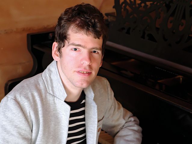 Grzegorz Płonka siedzi oparty o klawiaturę fortepianu