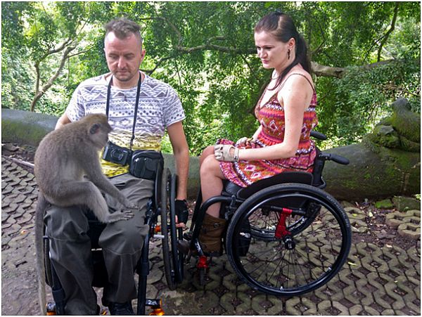 Małpa siedzi na kolanach mężczyzny na wózku. Obok kobieta na wózku