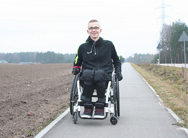 Rafał Miszkiel na wózku na asfaltowej drodze, obok jezdnia i pola