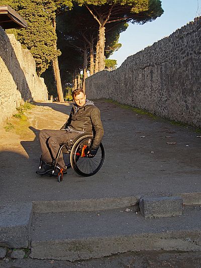 Mężczyzna na wózku na nierównej drodze wśród ruin