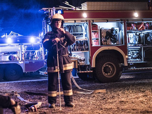 Niewidomy mężczyzna z białą laską w stroju strażaka stoi przed wozem strażackim