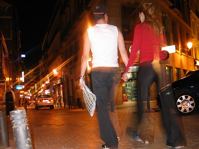 Kobieta i mężczyzna idą wieczorem ulicą miasta, trzymając się za ręce