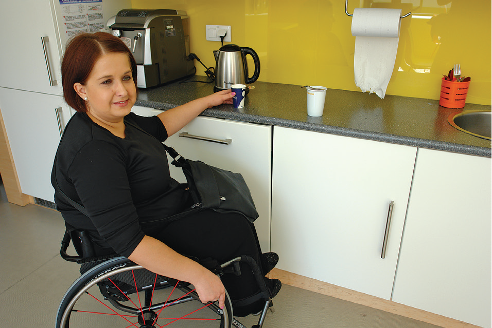 kobieta na wózku trzyma w dłoni kubek w kuchni, podczas swojej przerwy w pracy