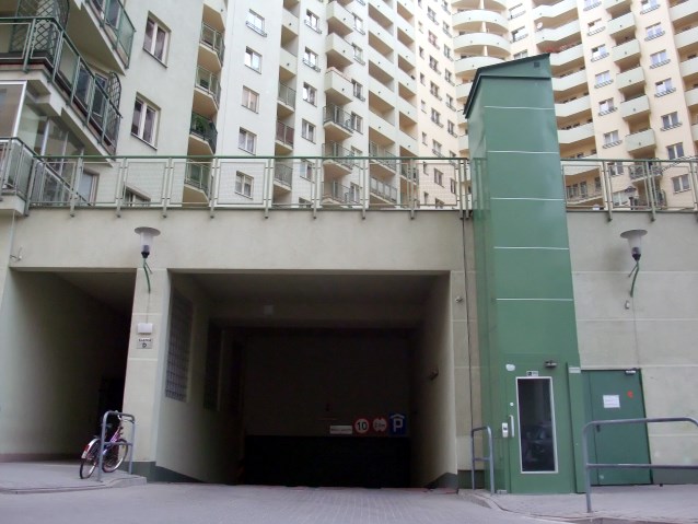 zielona winda dla osób z niepełnosprawnością, prowadząca z parkingu na teren bloku