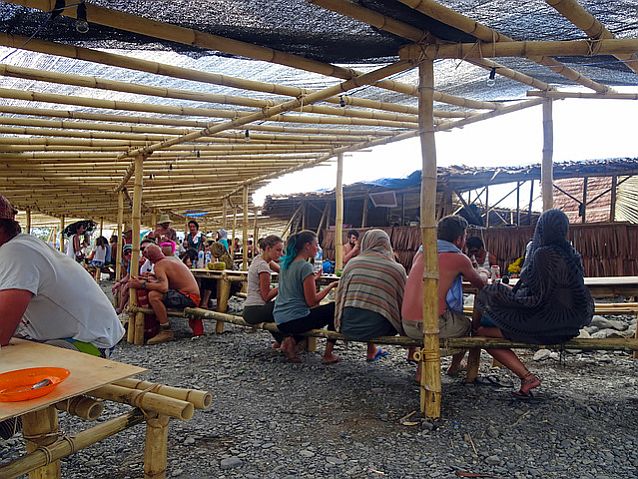 bambusowa konstrukcja z zadaszeniem, pod którą siedzą ludzie i jedzą posiłki
