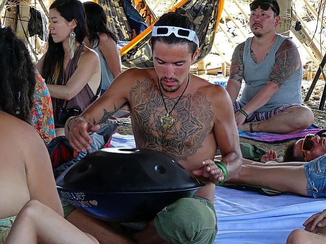 mężczyzna z tatuażem na piersi gra na tradycyjnym instrumencie, grającym przez uderzanie w niego palcami