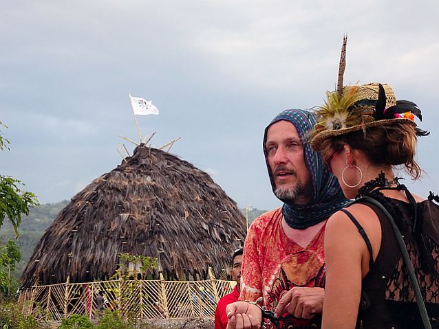 mężczyzna z kolorową chustą na głowie rozmawia z kobietą w kapeluszu ozdobionym piórami