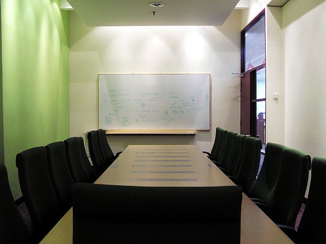 Pusta salka konferencyja, wokół stołu puste krzesła, w tle zapisana tablica