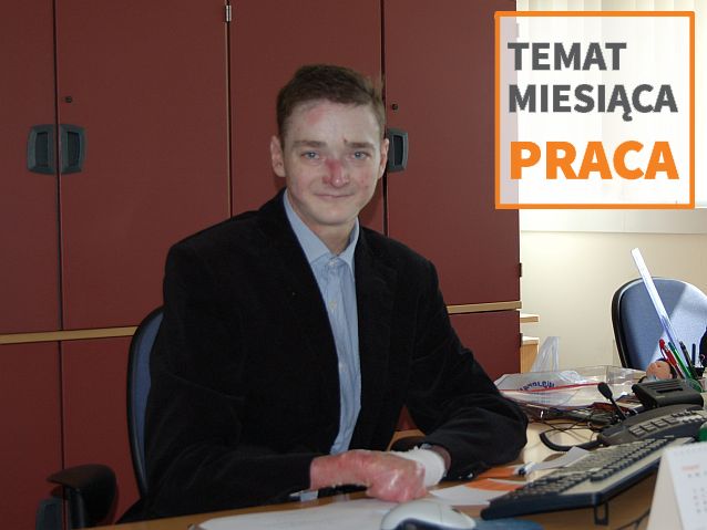 Przemysław Sobieszczuk siedzi przy biurku w pracy. Na zdjęciu także napis: Temat miesiąca Praca