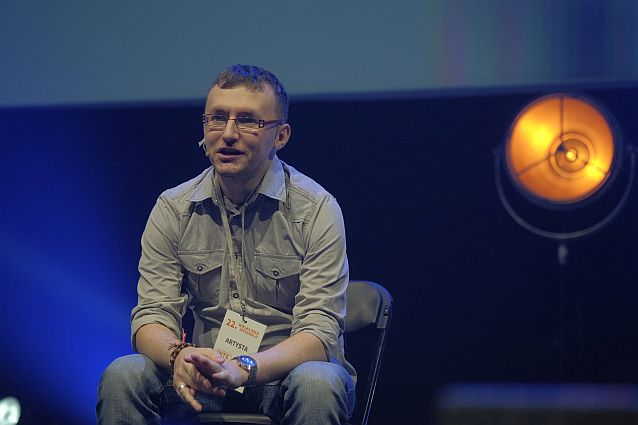 Jacek Noch siedzi na krześle w czasie swojego występu i mówi do mikrofonu