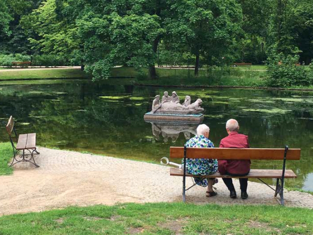 Kobieta z kulą i mężczyzna siedzą na ławce nad wodą w parku