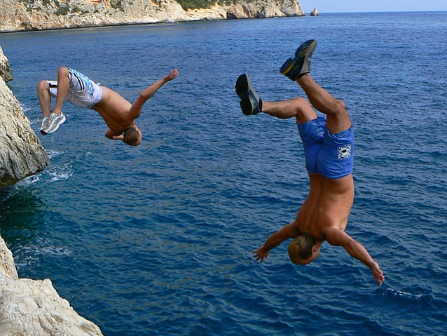 Dwaj mężczyźni skaczą ze skał do wody, w locie są obróceni do góry nogami