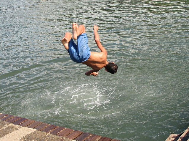 Młody mężczyzna odwrócony plecami do wody podczas skoku z pomostu