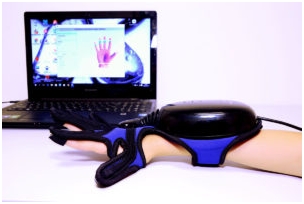 Ręka w przypiętej do wszystkich palców rodzaju uprzęży, w tle laptop z wyświetloną na ekranie dłonią