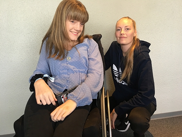Zdjęcie przedstawia dwie młode kobiety. Marianne na wózku pozuje do zdjęcia z kucająca obok Annicken