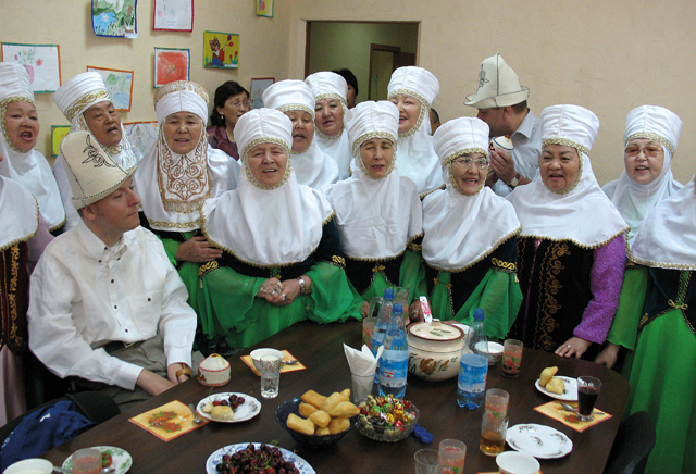 Piotr Pawłowski w otoczeniu kobiet w średnim wieku, które śpiewają, są w tradycyjnych strojach kazachstańskich
