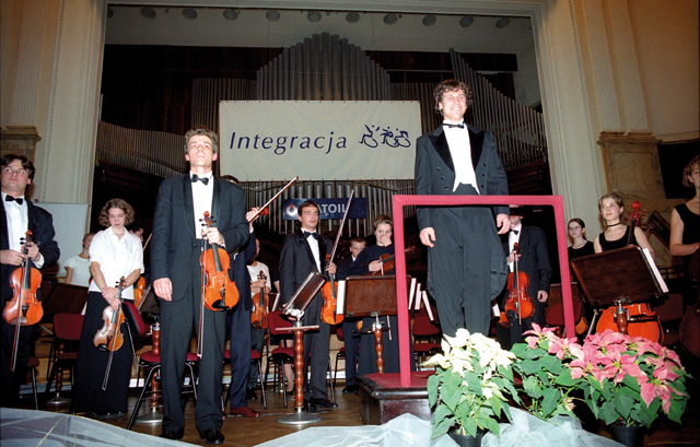 Wielka Gala Integracji - uśmiechnięty dyrygant, za nim orkiestra.