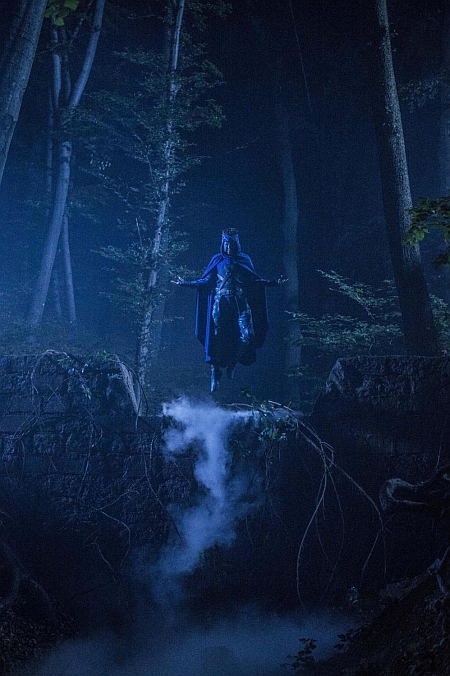 Chłopiec w stroju superbohatera unosi się nad ziemią w ciemnym lesie