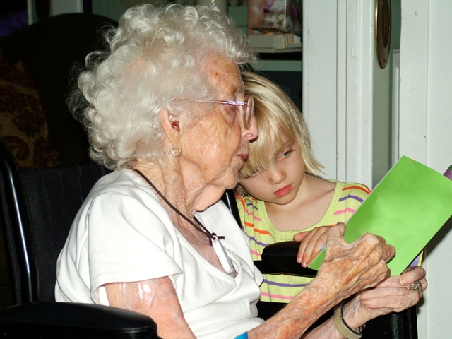 babcie siedzi na wózku i czyta przytulonej do niej dziewczynce książkę