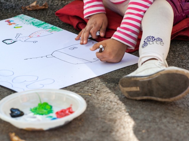 dziecko siedzi na podłodze i rysuje rodzinę, widoczne tylko do pasa z kredką w ręce