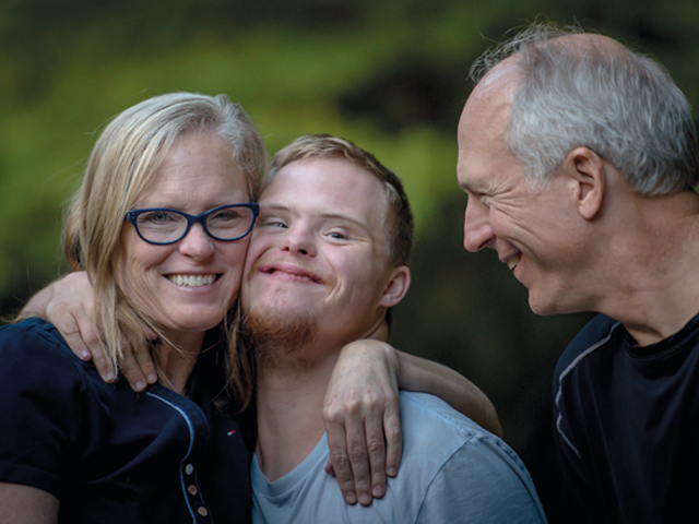 uśmiechnięci rodzice przytulają młodego mężczyznę z zespołem Downa