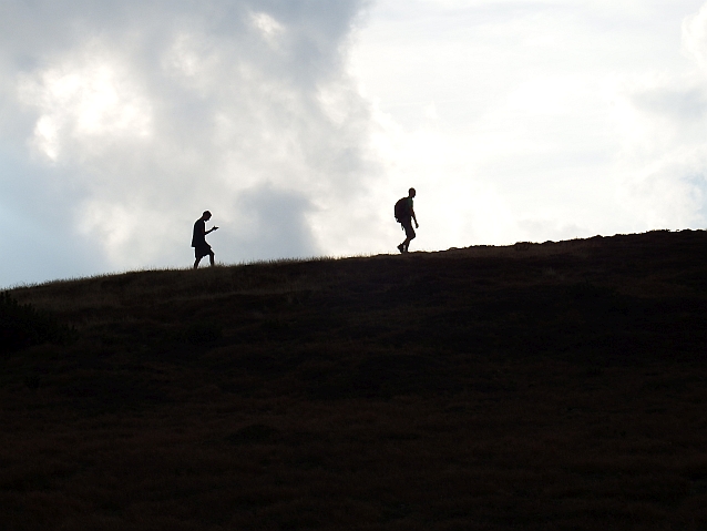 Dwóch mężczyzn idzie w pewnym oddaleniu od siebie po grani wzgórza w górę