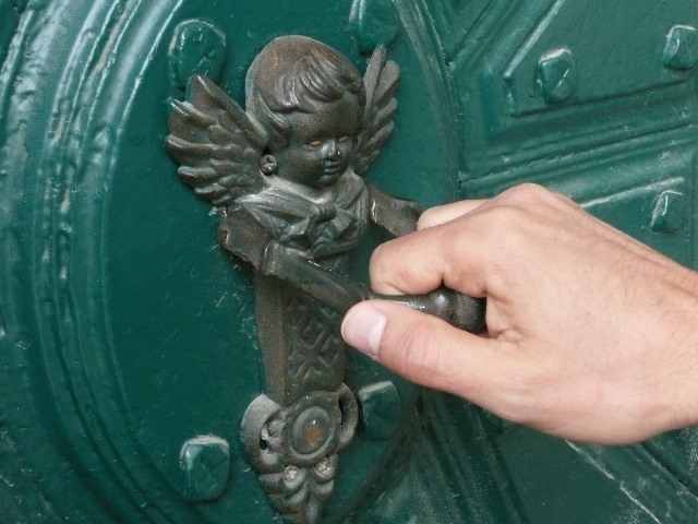 ręka uderza kołatką w kształcie anioła w drzwi wejściowe
