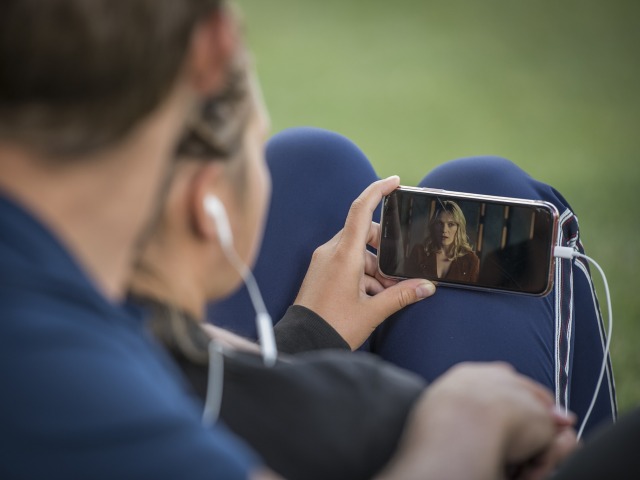 kobieta i mężczyzna w słuchawkach w uszach oglądają film na smartfonie