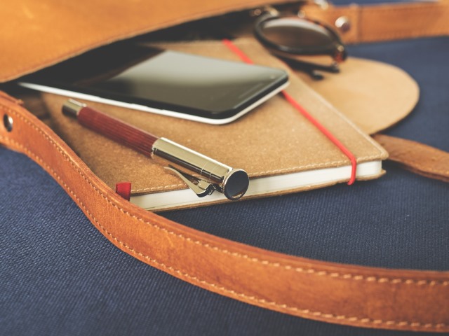 z leżącej torby wystaje notatnik, smartfon, długopis