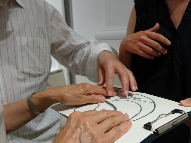 mężczyzna dotyka rysunku, który ktoś trzyma mu przypięty na podkładce biurowej