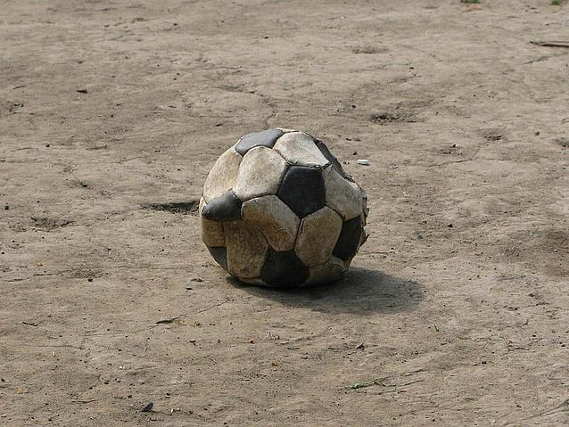 Pęknięta piłka futbolowa leży na piaszczystym boisku