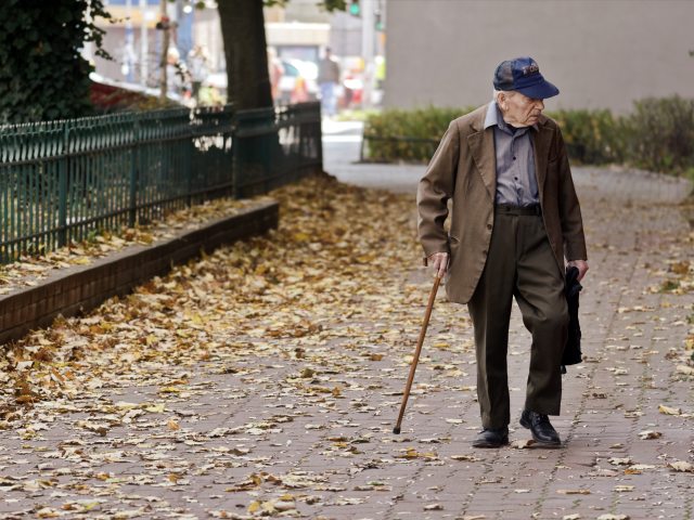starszy meżczyzna z laską idzie chodnikiem leżą jesienne liście