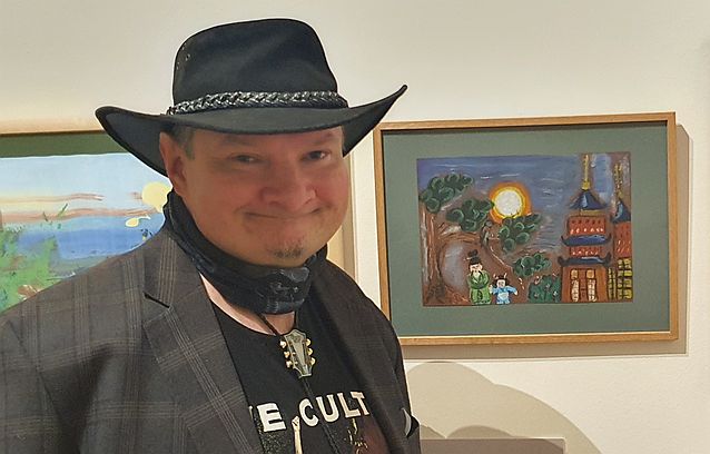 Uśmiechnięty Stanisław Kmiecik pozuje do zdjęcia. W tle wiszący na ścianie obraz